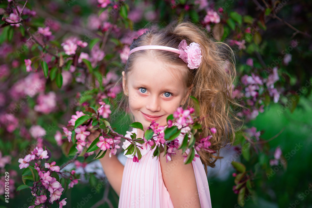 Beautiful smiling cute girl with long curly hair in blooming pink apples Beautiful smiling cute girl with long curly hair in blooming pink apples