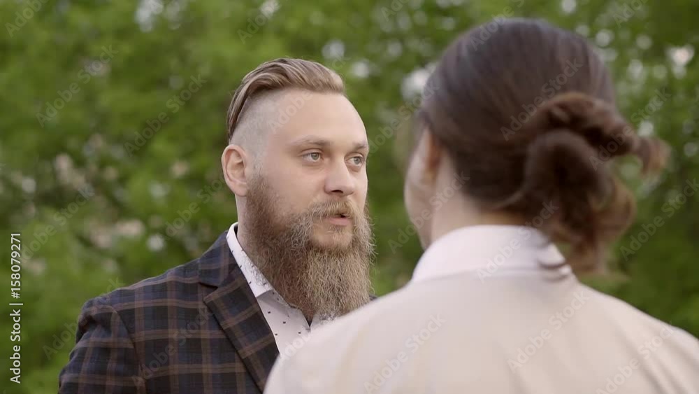 successful stylish young man with fashionable haircut and beard talking with a woman. the woman stands back, look at the man over her shoulder successful stylish young man with fashionable haircut and beard talking with a woman. the woman stands back, look at the man over her shoulder