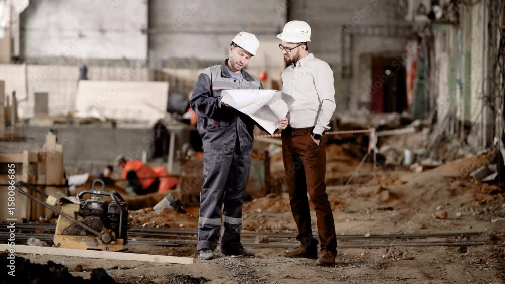 The engineer shows the customer in a protective helmet the estimate of a new building in order to amend its reconstruction The engineer shows the customer in a protective helmet the estimate of a new building in order to amend its reconstruction