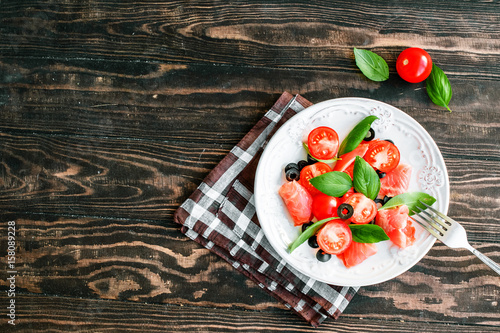 salad with salmon  basil  tomatoes and olives in bowl on napkin and wooden table