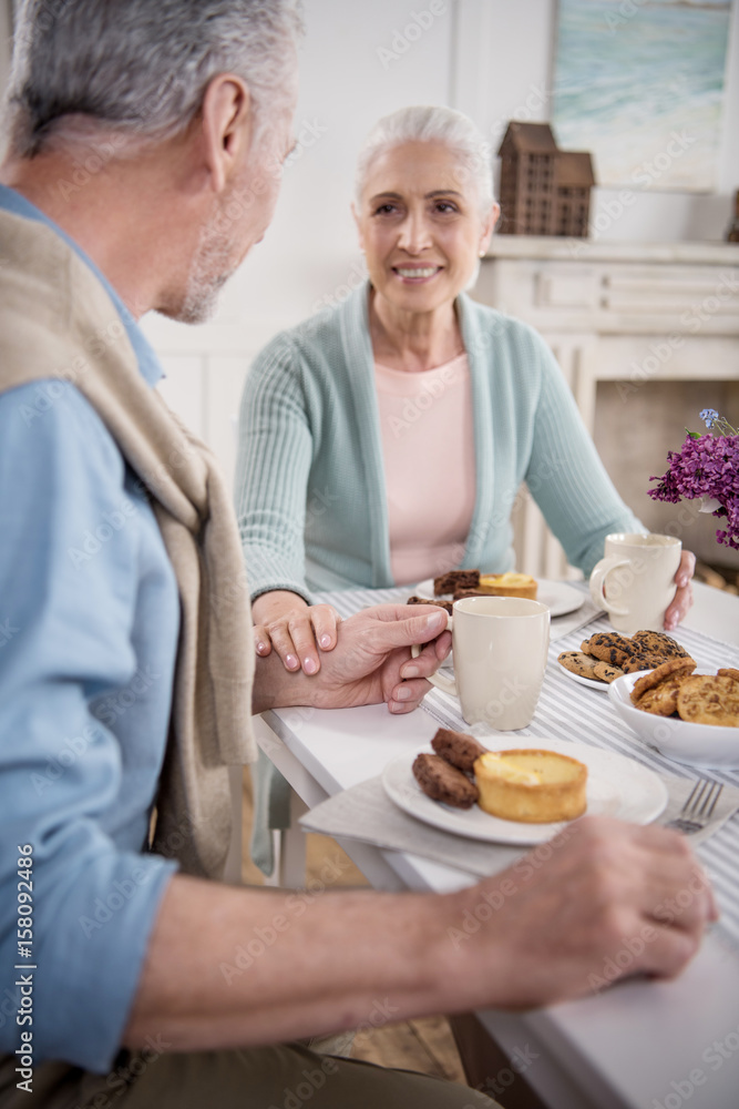 elderly couple holding hands while having breakfast at home elderly couple holding hands while having breakfast at home