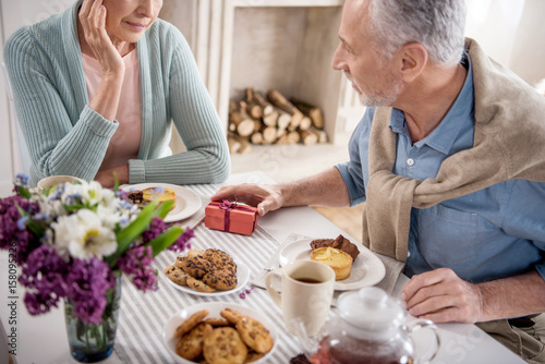 cropped shot of grey haired man presenting gift to his wife during breakfast