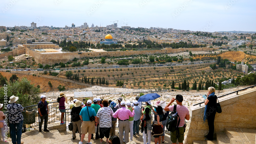 Fototapeta premium The guide shows the Jerusalem Old City view to the tourists. Mount of Olives is a famous and sacred Christian's place and it has a fantastic view to the Old Jerusalem.