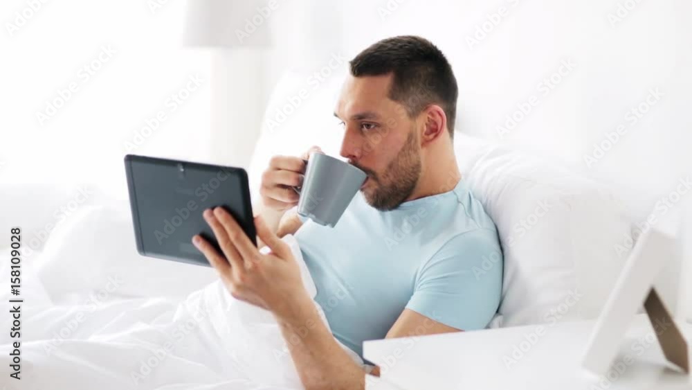 man with tablet pc drinking coffee in bed at home man with tablet pc drinking coffee in bed at home