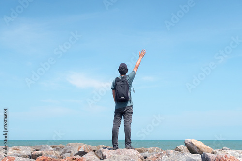 Photography Traveler standing and raising his hand on the rock starring at the sea