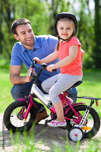 Girl learning to ride a bicycle with father   © pikselstock