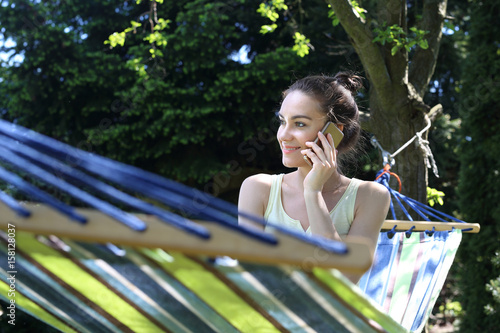 Relaks w ogrodzi.Kobieta rozmawia przez telefon siedząc w hamaku