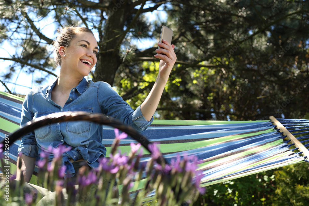 Chilout w ogrodzie.Młoda atrakcyjna kobieta wypoczywa na hamaku w ogrodzie rozmawiając przez telefon - obrazy, fototapety, plakaty 