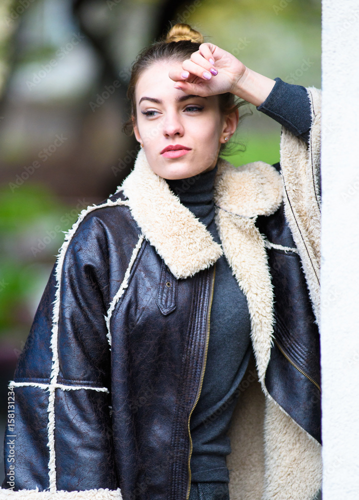 A stunning female model dressed in a leather poncho and tweed trousers walking through the European city at spring. Urban fashion blogger posing with a trendy 2017 look.
