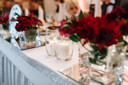 White candles put in vases stand between red flowers