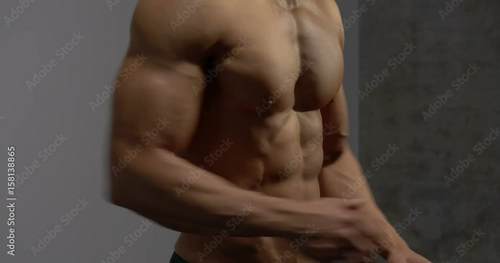 The muscular torso of a fitness model is filmed from profile with a slight angle. He prepares for a work out and crosses his arms.