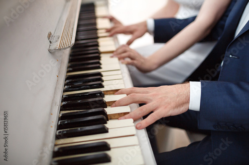Bride and groom play on white piano