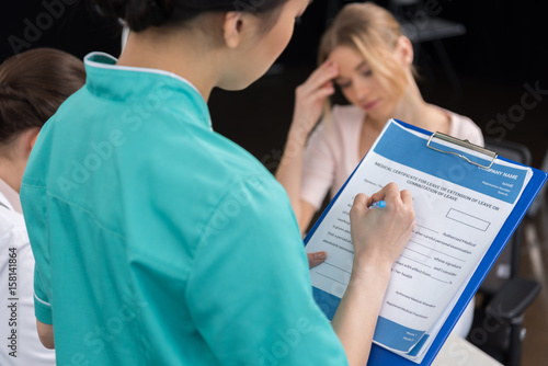 internist filling medical form while patient sitting behind in clinic photo