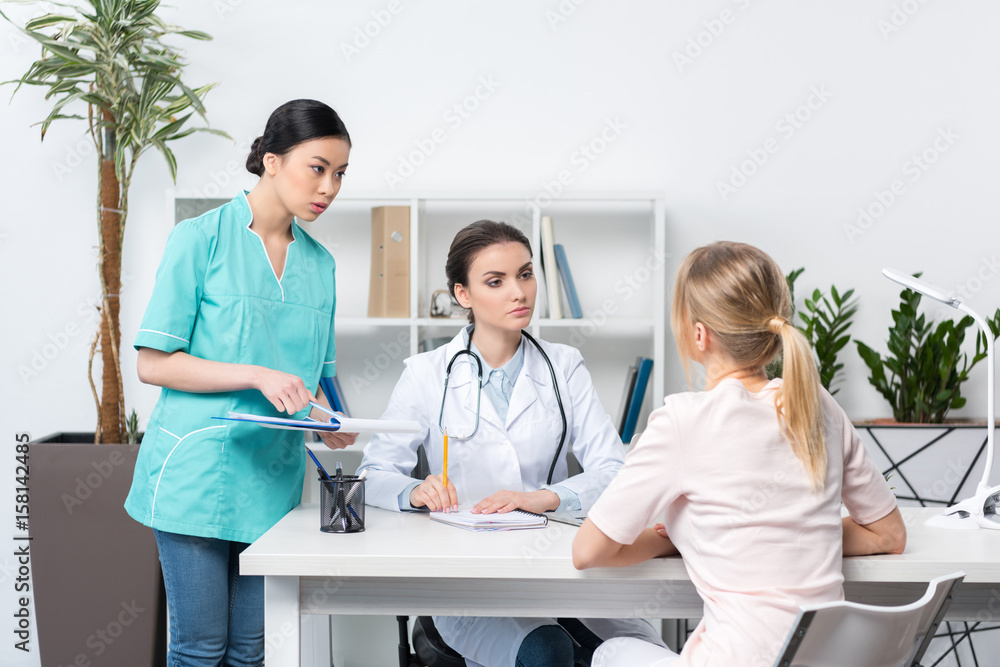 Fototapeta premium Young patient sitting in chair and talking with doctor and nurse in medical office