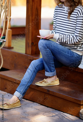 Cup of coffee in hands woman which sits on the wooden steps