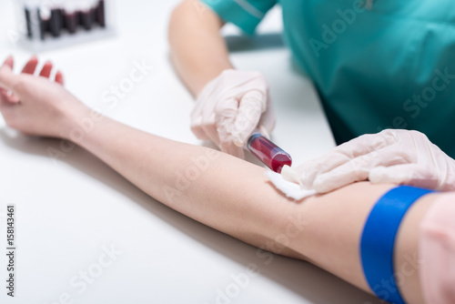 cropped shot of nurse taking blood sample of patient with syringe