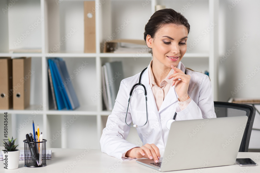 pensive young caucasian doctor looking at laptop screen while sitting at table in professional clinic pensive young caucasian doctor looking at laptop screen while sitting at table in professional clinic