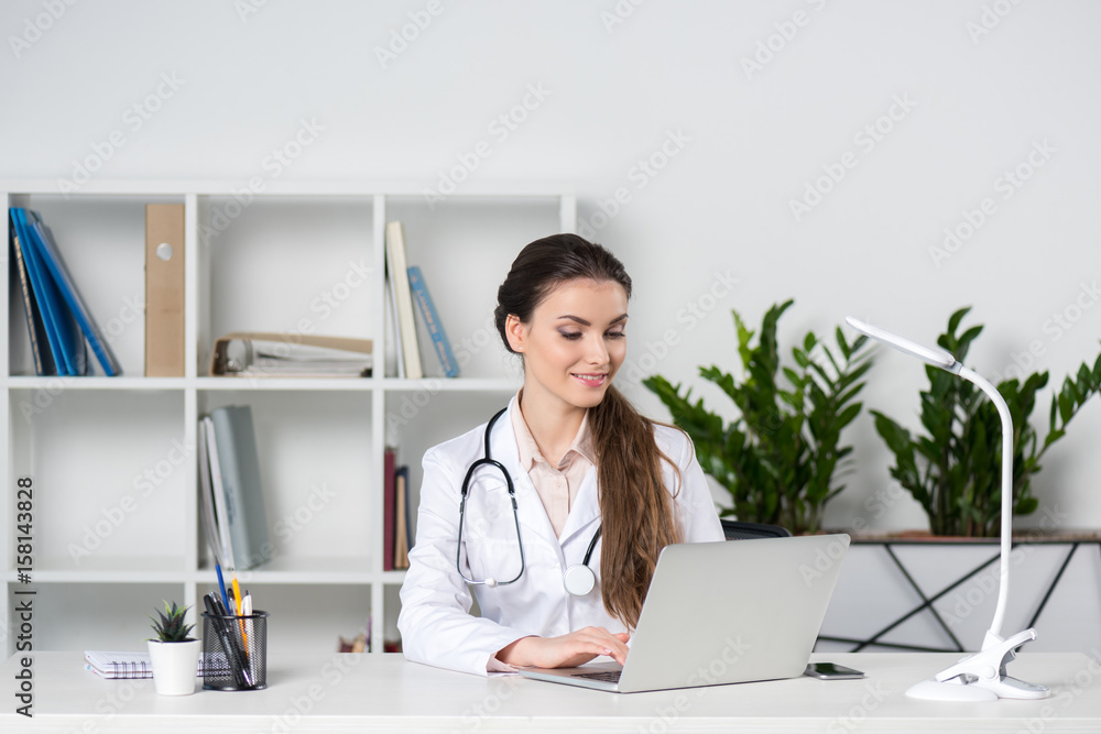 young caucasian doctor working and typing in laptop while sitting at table in clinic young caucasian doctor working and typing in laptop while sitting at table in clinic