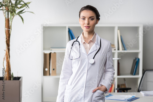 young caucasian doctor with stethoscope standing and looking at camera in clinic
