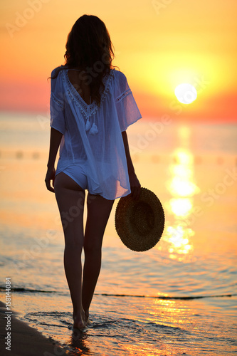 Slim woman walking on the beach at sunset