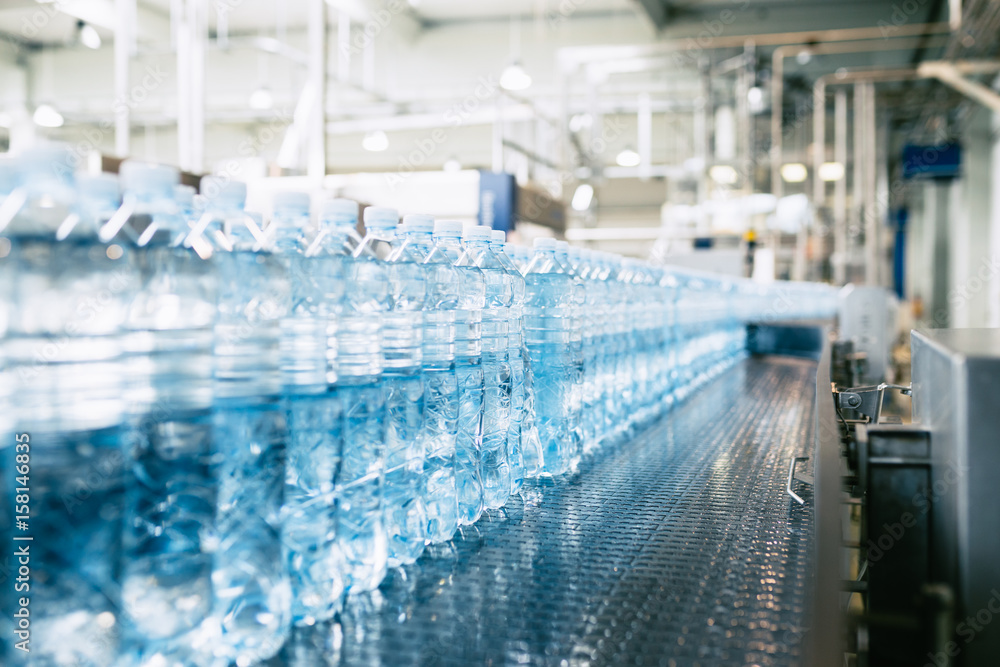 Bottling plant - Water bottling line for processing and bottling pure spring water into blue bottles. Selective focus. Bottling plant - Water bottling line for processing and bottling pure spring water into blue bottles. Selective focus.