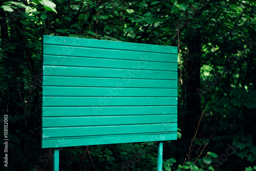 A wooden green billboard stands in the middle of the forest. copy space