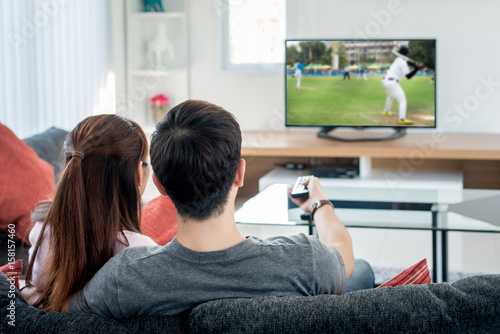 Young Asian couple waching baseball sport on tv at home