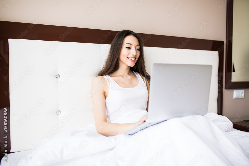 Portrait of beautiful young woman with laptop on bed in the morning Portrait of beautiful young woman with laptop on bed in the morning