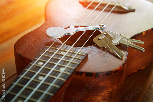 Key with keychain in form of guitar put on the ukulele, close up view