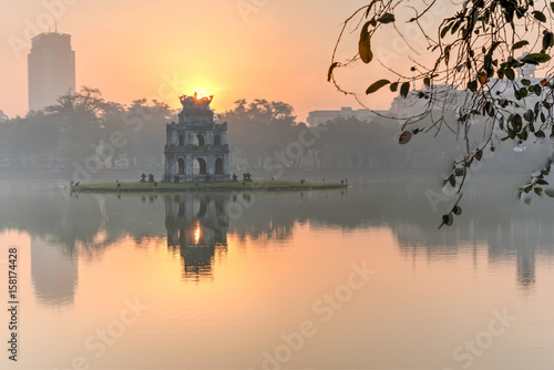 Fototapeta Naklejka Na Ścianę i Meble -  Sun rising behind the Turtle Tower in the center of Hoan Kiem Lake (Lake of the Returned Sword). The lake is one of the major scenic spots in the city and serves as a focal point for its public life.