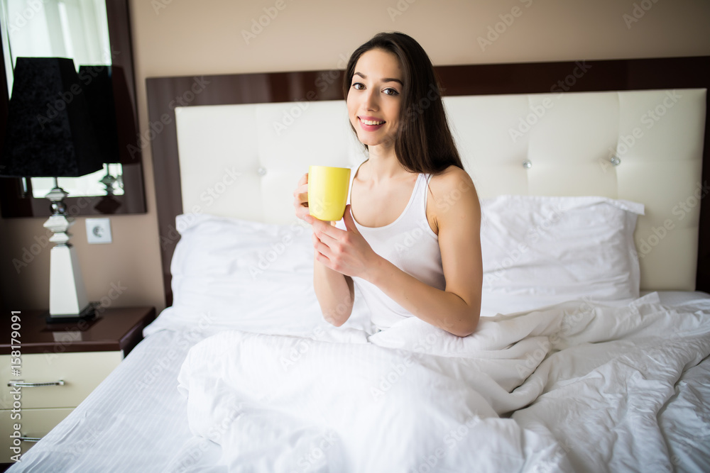 Beautiful woman drinking a coffee sitting on her bed at home in the morning Beautiful woman drinking a coffee sitting on her bed at home in the morning