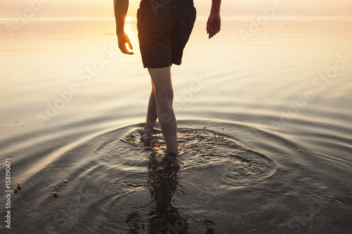 Man in shorts wading in sea at sunset photo