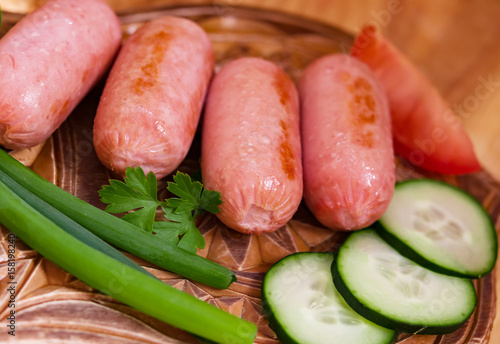 Breakfast fried mini sausages with vegetables on a light wooden table closeup