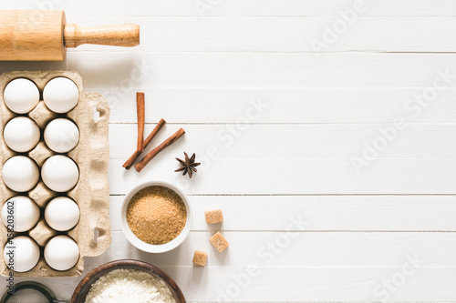 Fototapeta Naklejka Na Ścianę i Meble -  Baking ingredients on white wood with copy space. Eggs, brown sugar, white flour, spices and rolling pin on white wooden background. Top table top view. Cooking, baking background, recipe mock up