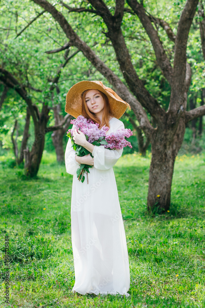 Redhead girl with a bouquet of lilacs in a spring garden
