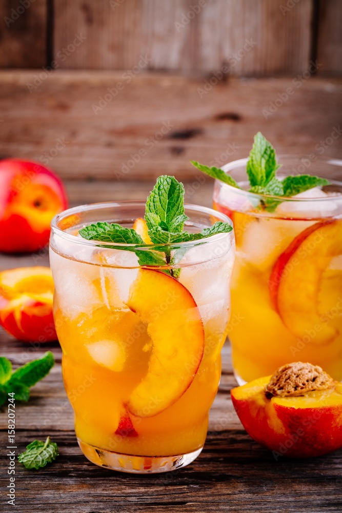 Summer cold drinks: homemade peach ice tea with ice cubes, and mint in glasses Summer cold drinks: homemade peach ice tea with ice cubes, and mint in glasses