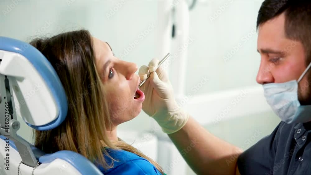 Examination at the dental clinic. Dentist using mouth mirror to provide a teeth check-up for the young woman patient Examination at the dental clinic. Dentist using mouth mirror to provide a teeth check-up for the young woman patient
