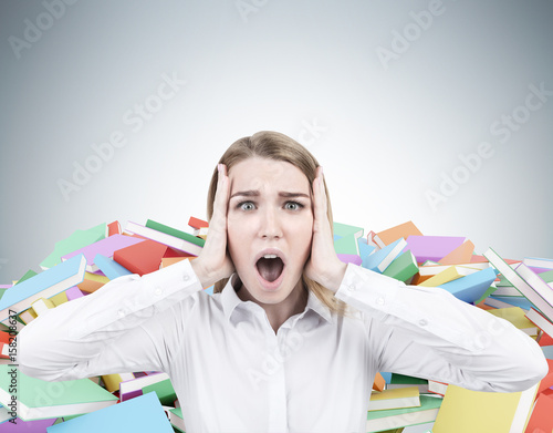 Blond businesswoman screaming, piles of books
