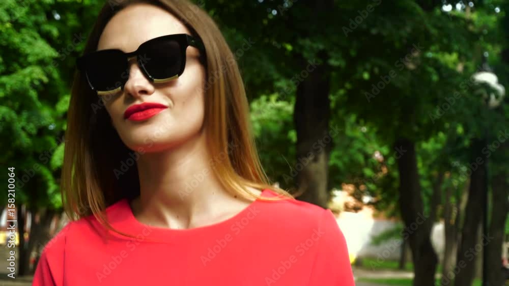 Handsome young woman in sunglasses with red lips walks outdoors Handsome young woman in sunglasses with red lips walks outdoors