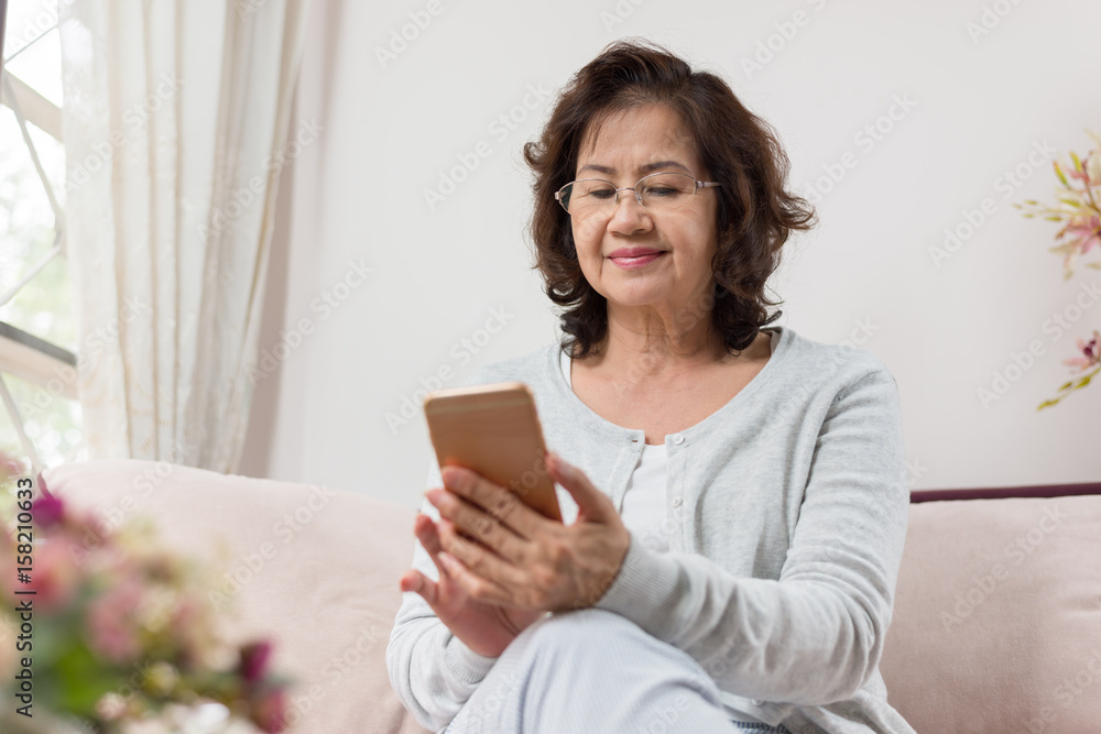 Happy Asian senior woman sitting on sofa and using a smart phone Happy Asian senior woman sitting on sofa and using a smart phone