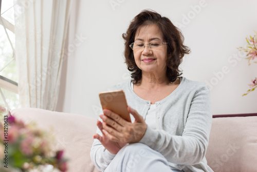 Happy Asian senior woman sitting on sofa and using a smart phone