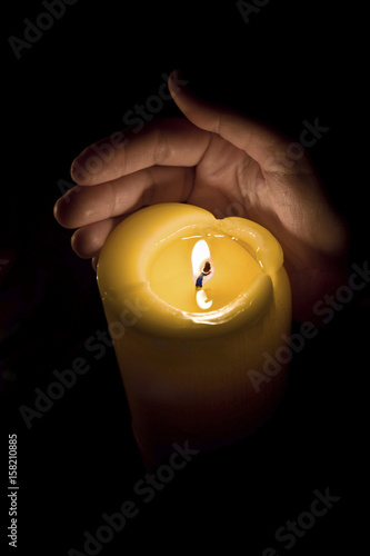 Hand protecting burning candle from wind