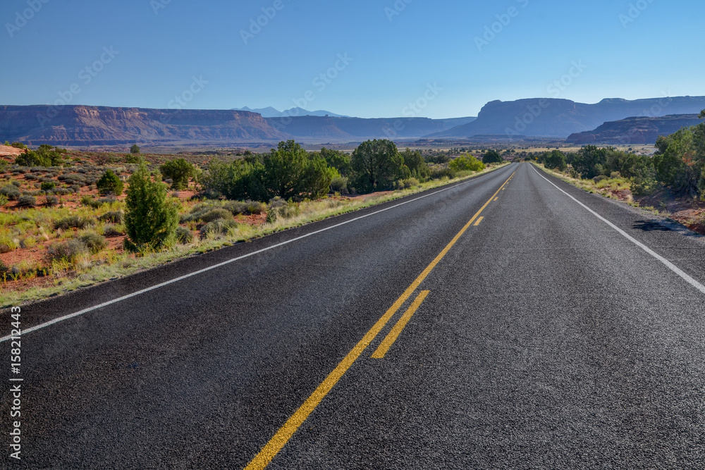 Naklejka premium empty country road in grasslands with flat top mountains in the background UT-211 Scenic Highway, Canyonlands National Park, Utah, United States