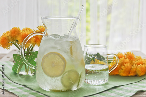 A jug of water and lemon and lime and a bouquet of dandelions