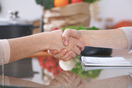 Close-up of shaking hands over a table in the kitchen. Friends having fun while choosing menu or making online shopping. So much ideas for tasty cooking. Vegetarian, healthy meal and friendship