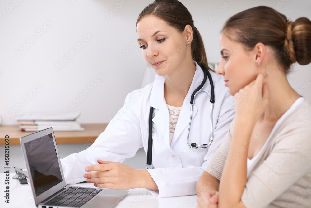 Doctor and patient sitting at the desk. Physician pointing into laptop computer. Medicine and health care concept Doctor and patient sitting at the desk. Physician pointing into laptop computer. Medicine and health care concept