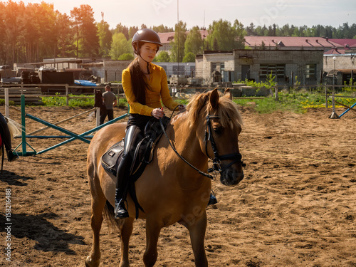 Young cheerful girl rides on a brown horse. Riding training. Horseback Riding.