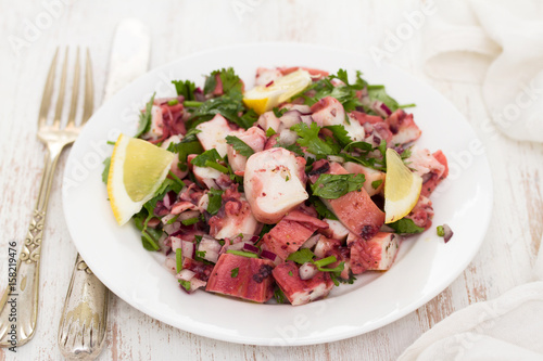 octopus salad with lemon on white dish on wooden background