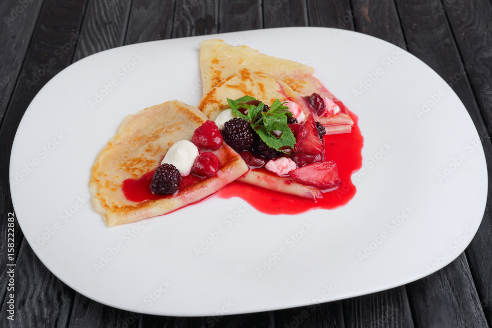 Plate with pancakes decorated with marshmallows, strawberry and dewberry, with syrup and mint leaves