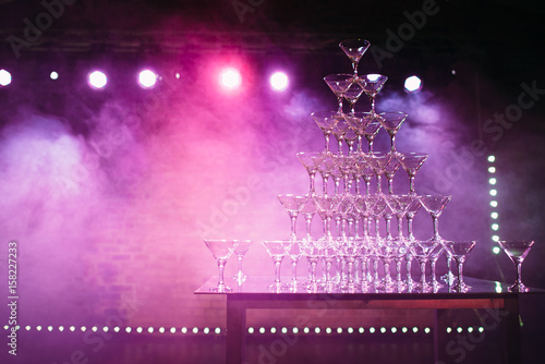 the pyramid of glasses with champagne on the wedding party. The smoke and light show. Background holiday themes